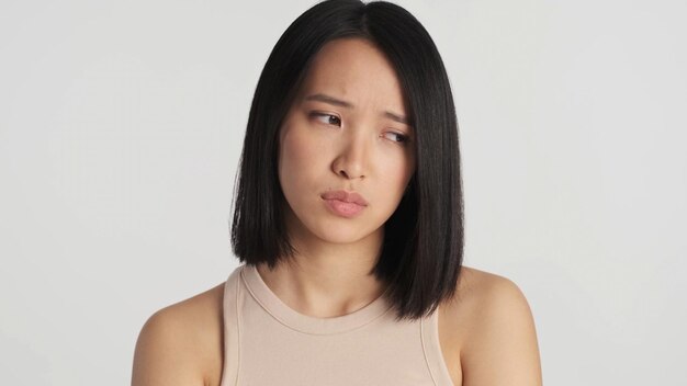 Close-up van trieste Aziatische vrouw die er depressief uitziet en over een witte achtergrond staat Ontevreden gezicht