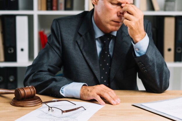 Close-up van uitgeputte mannelijke rijpe advocaatzitting voor bureau