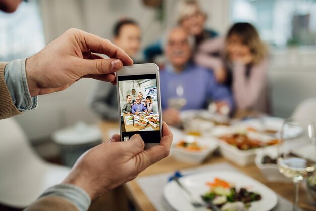 Close-up van vader die mobiele telefoon gebruikt en een foto maakt van zijn familie van meerdere generaties in de eetkamer