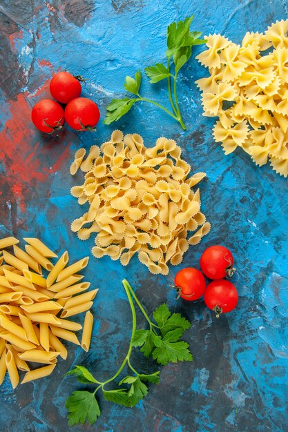 Close-up van verschillende rauwe Italiaanse pasta's die op een rij zijn gerangschikt en tomaten met stengel op blauwe achtergrond