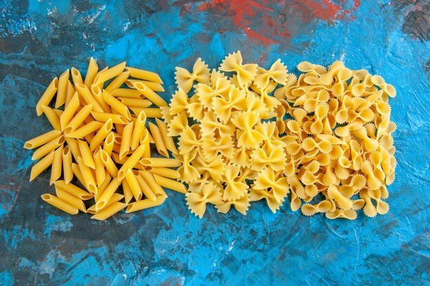 Close-up van verschillende rauwe Italiaanse pasta's gerangschikt in een rij op blauwe achtergrond