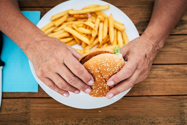 Close up van volwassen vrouw met een hamburger met frietjes op een houten tafel - fastfood en ongezonde levensstijl en concept