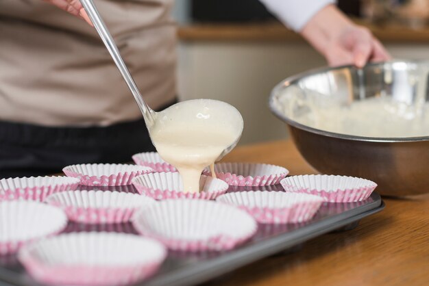 Close-up van vrouw gieten cakebeslag in de cupcake geval met pollepel