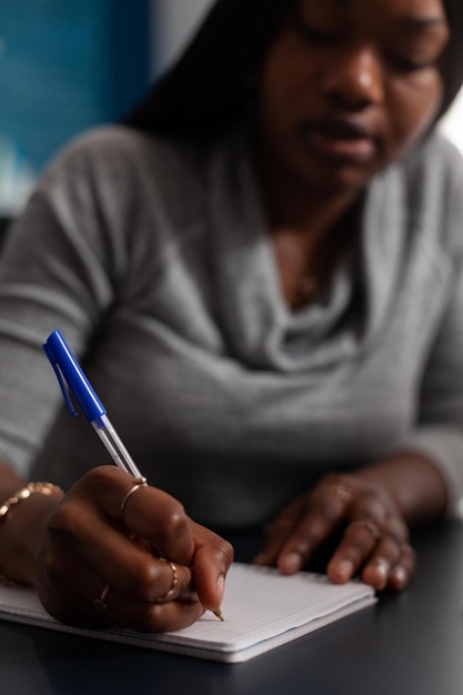 Close up van vrouw het maken van aantekeningen met pen op leerboek aan balie. Jonge volwassene schrijft informatie op notebookpapier terwijl hij vanuit huis werkt aan een zakelijk project. Persoon met werk op afstand