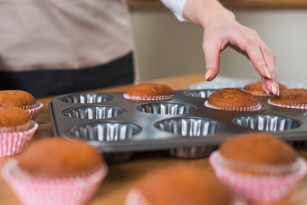 Close-up van vrouwelijke bakker die de cupcake verwijdert uit het muffindienblad