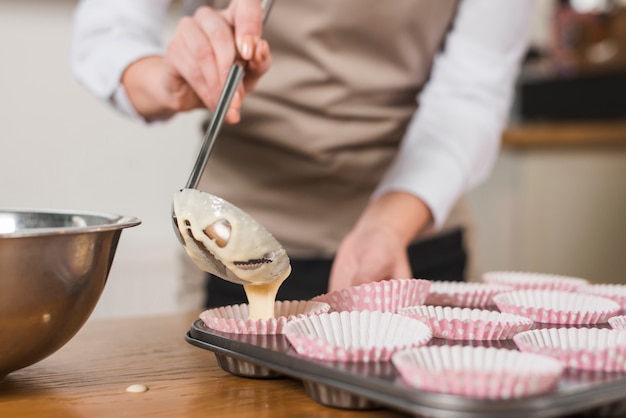 Close-up van vrouwelijke bakker gieten gemengde cakebeslag in de cupcake houder