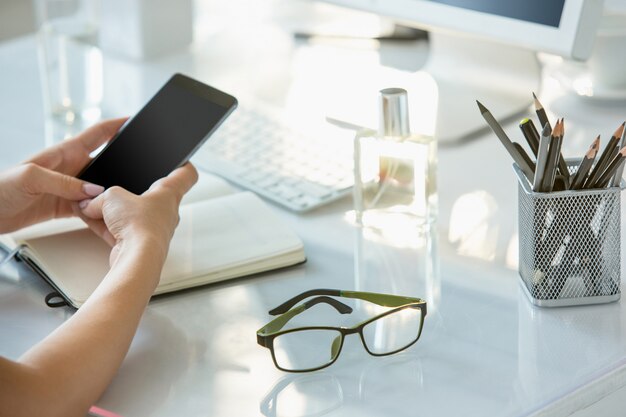 Close-up van vrouwelijke handen die telefoon met behulp van terwijl het werken aan computer op modern bureaubinnenland