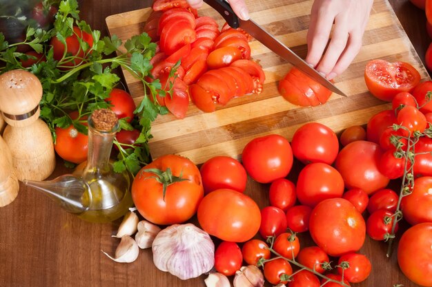 Close-up van vrouwelijke handen die tomaten snijden
