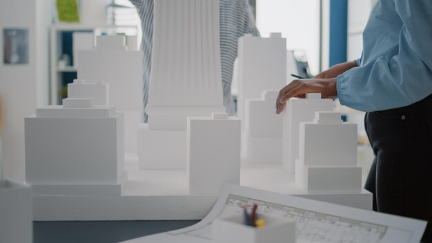 Close up van vrouwen met bouwmodel en blauwdrukken plan op tafel. Diverse architecten die met maquette en industriële schets werken om de constructiestructuur en het strategieproject te ontwerpen.