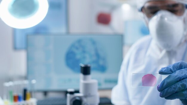 Close-up van wetenschapper-onderzoeker arts met medische dia die bloedmonster analyseert die werkt bij coronavirusvaccin tijdens scheikunde-experiment in biochemisch ziekenhuislaboratorium, virusonderzoek