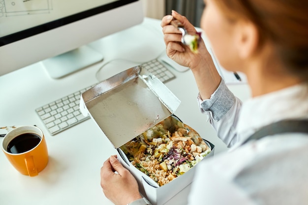 Close-up van zakenvrouw die een gezonde maaltijd eet terwijl ze op kantoor werkt