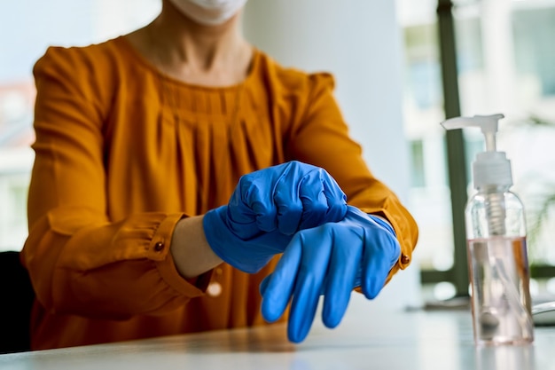 Close-up van zakenvrouw die haar handen beschermt met een handschoen terwijl ze op kantoor werkt tijdens een virusepidemie