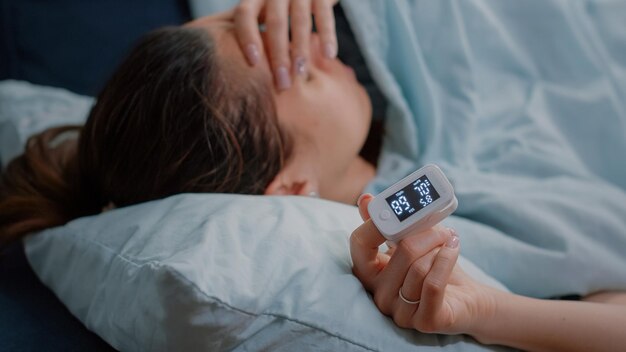 Close up van zieke hand van vrouw met oximeter op vinger gebruikt voor diagnose van de ziekte. Volwassene die een apparaat gebruikt om de verhoging van de zuurstofsaturatie en de polsdruk te meten. Persoon met verkoudheid en griep