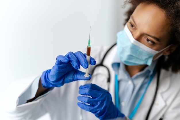 Close-up van zwarte vrouwelijke epidemioloog die spuit gebruikt bij medische kliniek