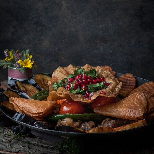 Close-up vlees met gebakken aardappelen, aubergine, tomaat, peper en versierd met granaatappel op houten schors