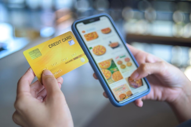 Close-up vrouw hand houdt creditcard (mock-up) online eten winkelen via slimme telefoon. online technologie bedrijfsconcept.