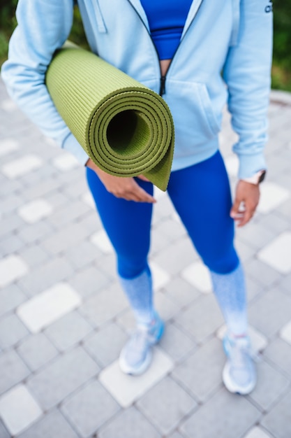 Gratis foto close-up vrouw met roll fitness of yoga mat na het trainen in het park.