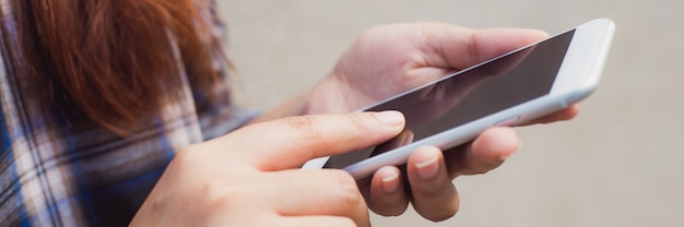 Gratis foto close-up vrouwelijke hand met behulp van slimme mobiele telefoon met leeg scherm op betonnen muur achtergrond. vintage effect stijl foto's. panoramische banner.