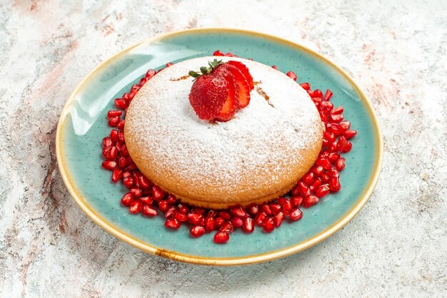 Gratis foto close-up zijaanzicht aardbei granaatappel plaat van cake met aardbeien en granaatappel op de roze-grijze tafel