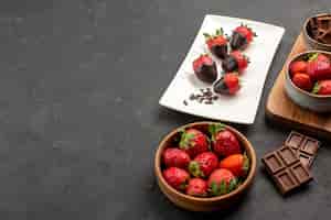 Gratis foto close-up zijaanzicht aardbeien aan boord van chocoladeroom en aardbeien op het bord naast het bord met chocolade omhulde aardbeien en schaal met aardbeien