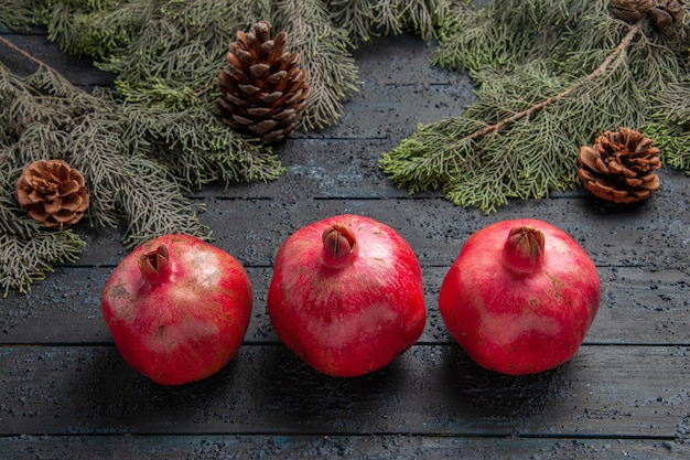 Close-up zijaanzicht granaatappels op tafel drie rijpe granaatappels naast boomtakken met kegels in het midden van de tafel