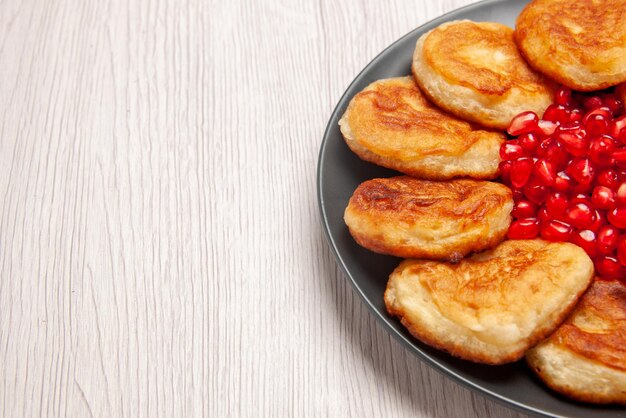 Close-up zijaanzicht pannenkoeken granaatappel en pannenkoeken op de zwarte plaat op de witte tafel