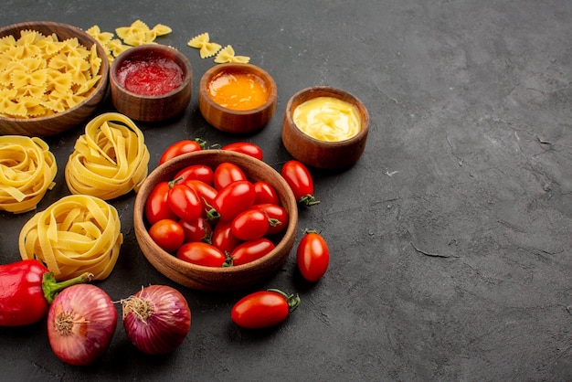 Close-up zijaanzicht pasta en tomaten paprika knoflook drie soorten sauzen ui en kommen pasta en tomaten op tafel