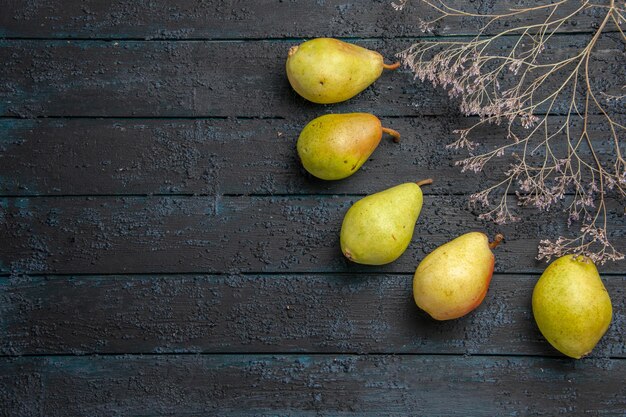 Close-up zijaanzicht vijf peren vijf groene peren aan de rechterkant van de donkere tafel naast de boomtakken