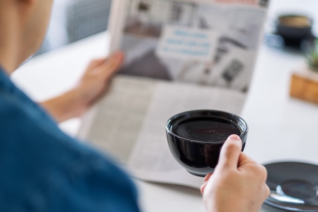 Close-upbeeld van een man die de krant leest en 's ochtends koffie drinkt