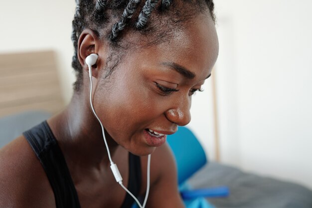 Close-upbeeld van jonge zwarte vrouw die zweterig is na thuis trainen en het volgende nummer op smartphone of speler kiest