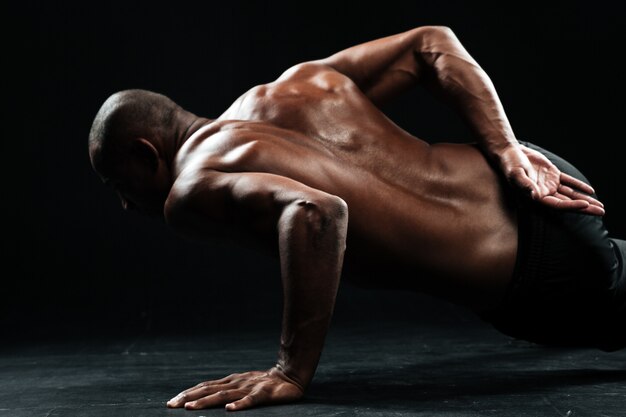 Close-upfoto van afro Amerikaanse mannelijke atleet die opdrukoefeningen met één hand doen