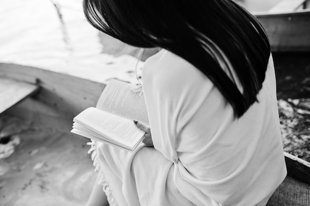 Close-upfoto van de rug van de vrouw tijdens het lezen van een boek in een boot zwart-witfoto