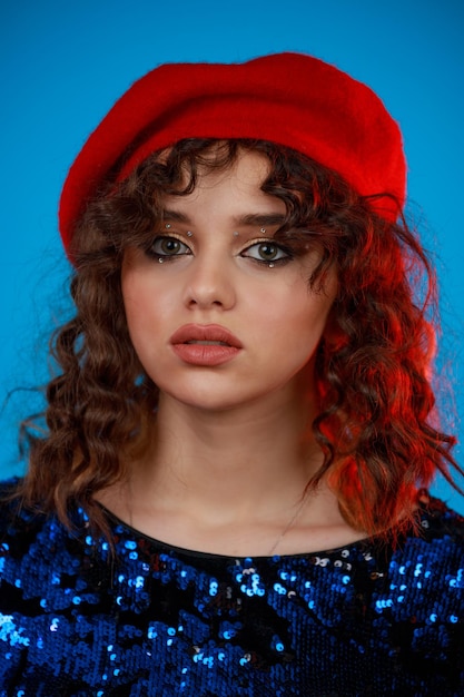 Close-upfoto van een jonge dame die een rode hoed draagt en naar de camera kijkt op een blauwe achtergrond foto van hoge kwaliteit Gratis Foto