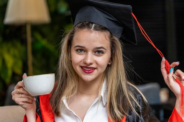 Close-upfoto van jonge studenten die een afstudeerpet dragen en een kopje thee vasthouden