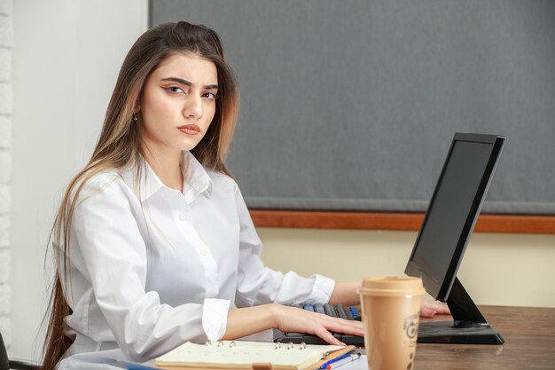 Close-upfoto van jonge zakenvrouw die achter het bureau zit en naar de camera kijkt