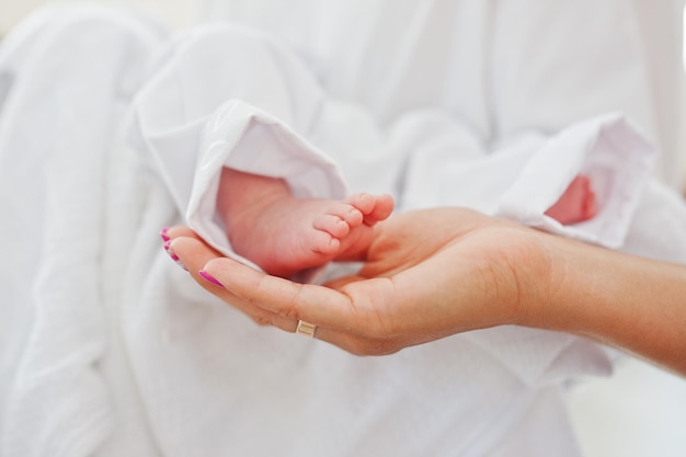 Close-upfoto van kleine benen van een pasgeboren baby op de handen van de moeder