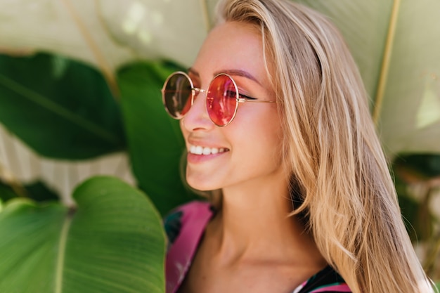 Close-upfoto van onbezorgde blonde vrouw draagt mooie roze zonnebril.