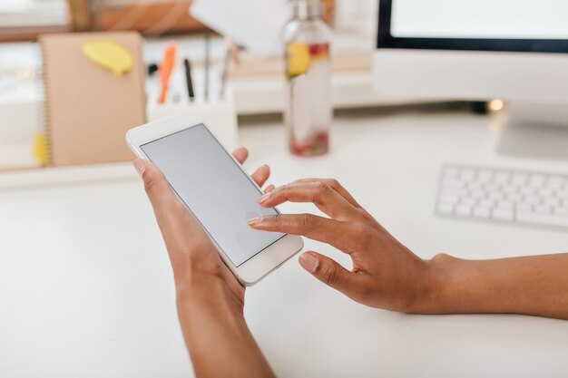 Close-upfoto van vrouwelijke handen die witte telefoon onder lijst houden