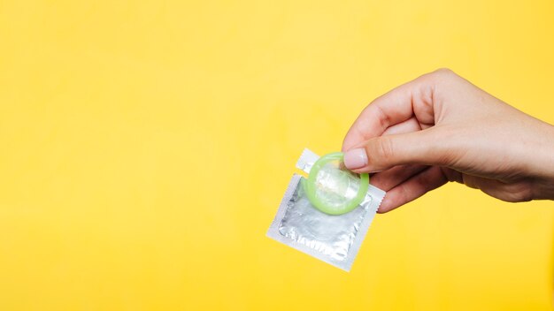 Close-uphand die een condoom met gele achtergrond houden