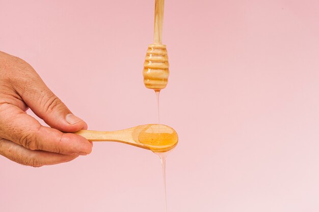Close-uphand die houten lepel met honing houden