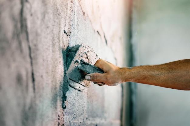 Close-uphand van arbeider die cement aan muur pleistert voor het bouwen van huis