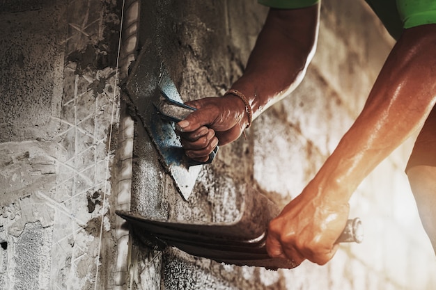 Close-uphand van arbeider het pleisteren cement bij muur voor de bouw van huis