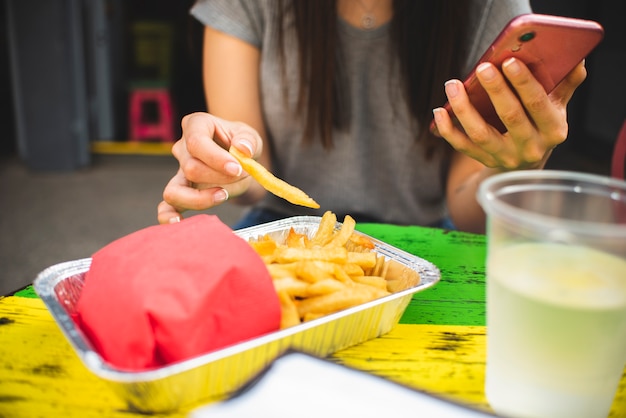 Close-upmeisje die met telefoon frieten eten
