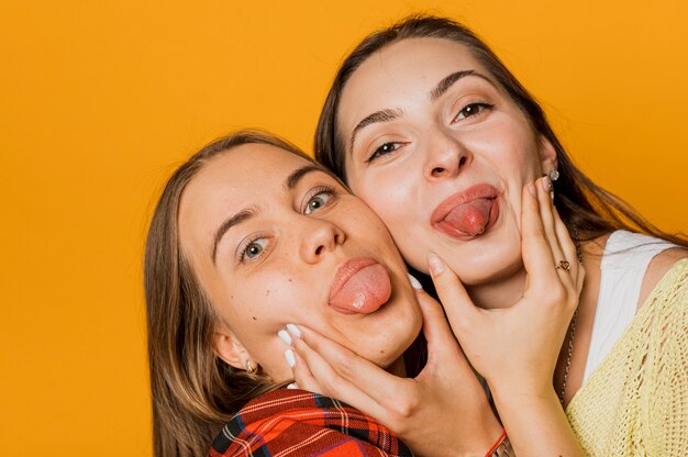 Close-upmeisjes met uit tongen en oranje achtergrond