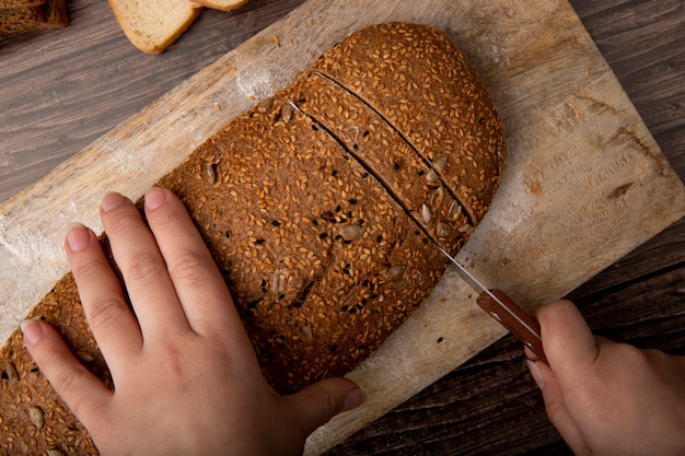 Close-upmening van vrouwenhanden die sandwichbrood met mes op scherpe raad op houten achtergrond snijden