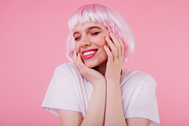 Close-upportret van aangenaam Kaukasisch meisje met trendy make-up poseren in roze peruke. Aantrekkelijk wit vrouwelijk model in korte periwig die tijdens fotoshoot lacht