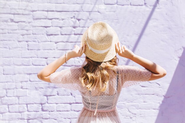 Close-upportret van achterkant van slank romantisch meisje in lichte kleding die oude muur bekijken