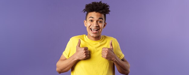 Close-upportret van enthousiaste gezonde Spaanse kerel die positief blijft, toont thumbsup en glimlacht enc