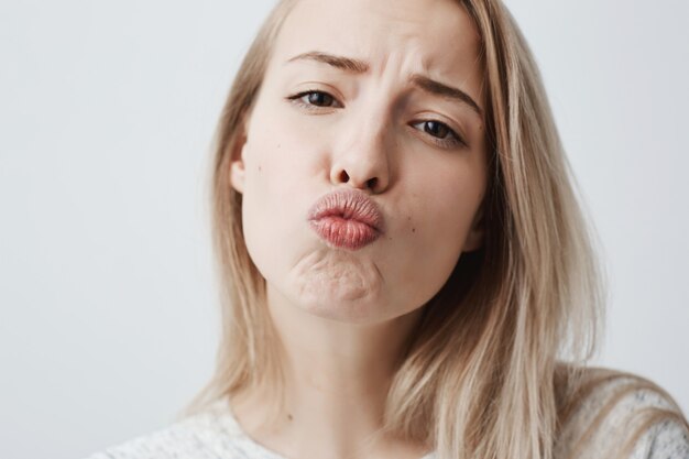 Close-upportret van het jonge aantrekkelijke Kaukasische vrouw stellen met kus op haar lippen met blond geverfd haar, die flirterig en zeker en mooi gevoel hebben. Charmant vrouwelijk model dat pret heeft binnen