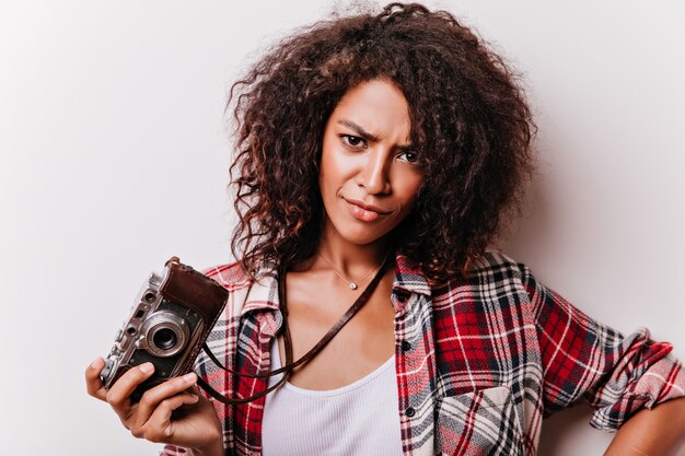 Close-upportret van ontevreden krullende vrouw met vintage camera. verbluffende vrouwelijke shotgrapher die zich in zelfverzekerde houding bevindt.